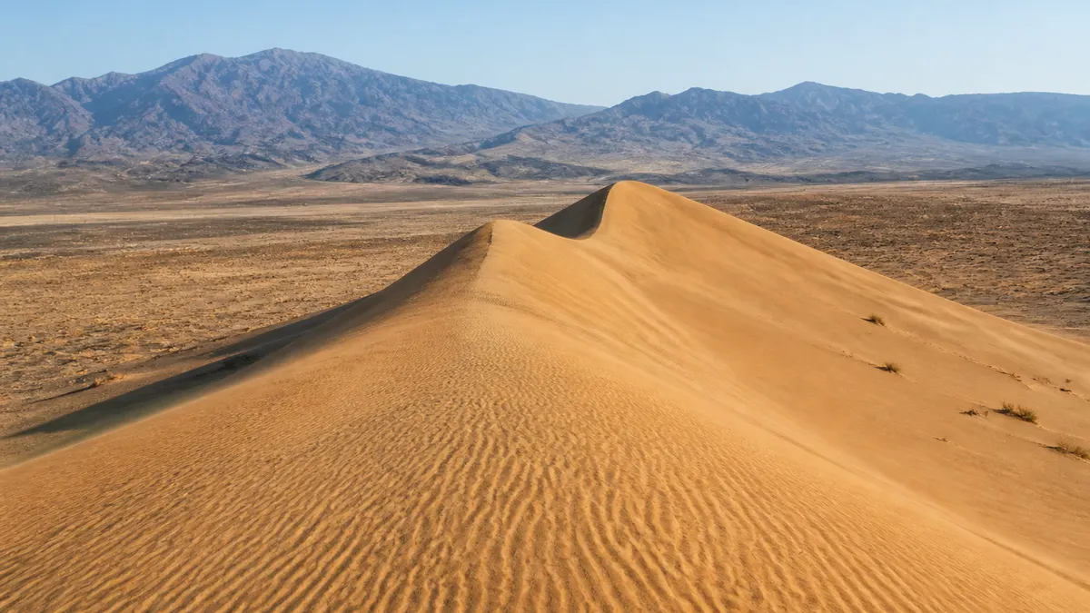 Wind-shaped golden ridge of the Singing Dune with dry steppe and mountains in Altyn-Emel National Park