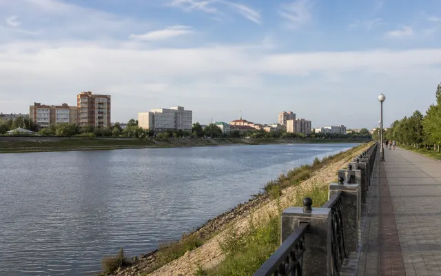 Conceptual contemporary Kostanay riverfront beside the Tobol with trees, an embankment and ordinary city buildings