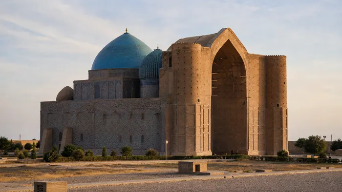 Conceptual early-morning view of the Khoja Ahmed Yasawi Mausoleum in Turkistan with brick walls and blue-tiled domes