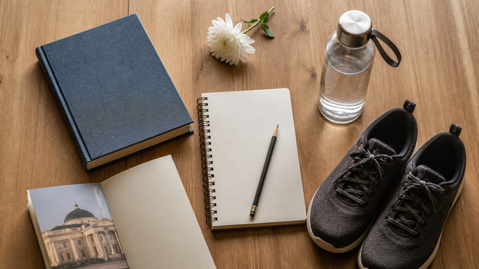 Conceptual Semey day-planning still life with a clothbound book, blank notebook, pencil, water bottle, walking shoes, an unlabelled museum brochure and a white flower