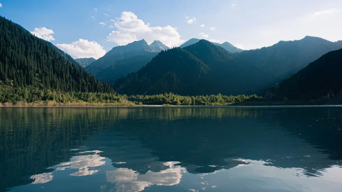 Summer view of Issyk Lake in Kazakhstan with wooded mountain slopes reflected in the water