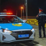 Kazakhstan police officer standing beside a patrol car at night, illustrating law enforcement presence in Kazakhstan.