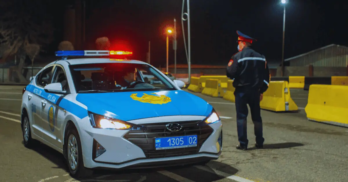 Kazakhstan police officer standing beside a patrol car at night, illustrating law enforcement presence in Kazakhstan.